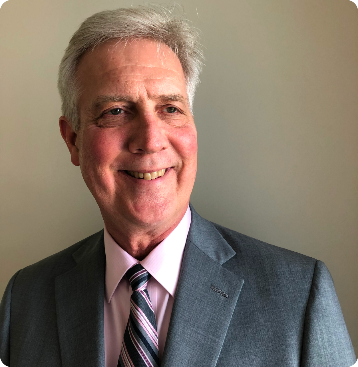 Smiling man in gray suit and pink shirt.